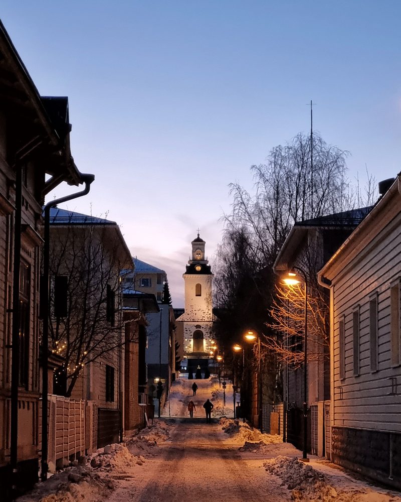 Snowy wooden town street at dusk with a church at the end